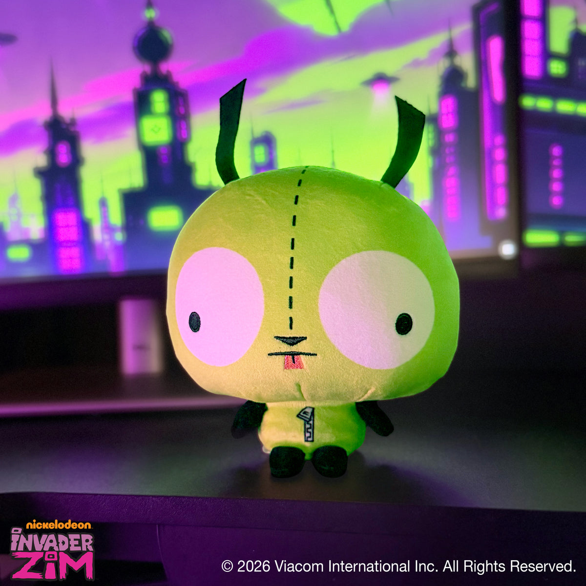 GIR Cloudheads plush sitting on a desk with a colorful green and purple cityscape in the background.