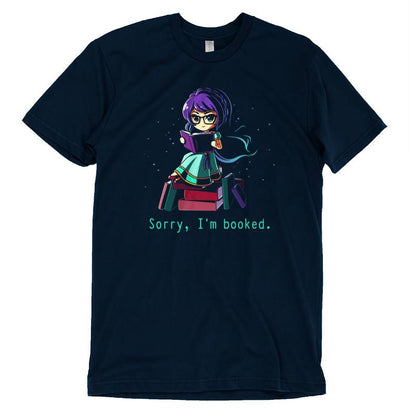 Unisex tee in navy blue featuring a cartoon character with purple hair reading a book, surrounded by more books. Made from super soft ringspun cotton. Text below reads, "Sorry I'm Booked." Product Name: Sorry I'm Booked. Brand Name: monsterdigital