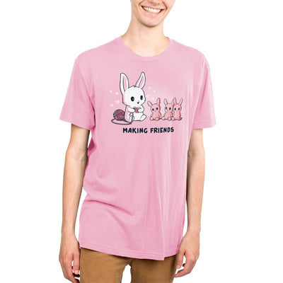Premium Cotton T-shirt_Teeturtle light pink Making Friends apparel featuring a white bunny knitting 3 bunny friends out pink of yarn, caption reads, "Making Friends'.