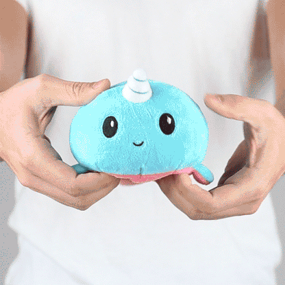 A person holding a TeeTurtle Reversible Narwhal Plushie (Pink + Aqua), showcasing their mood plushies collection.