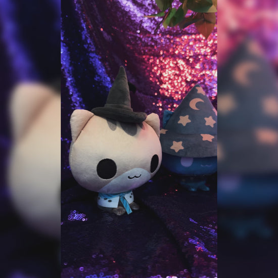 The whole set of 10 Mystic Moon Cloudheads plushies in front of a sparkly purple background. Also visible are books, a salt lamp, a crystal ball, an antique scale and a leafy green plant. 
