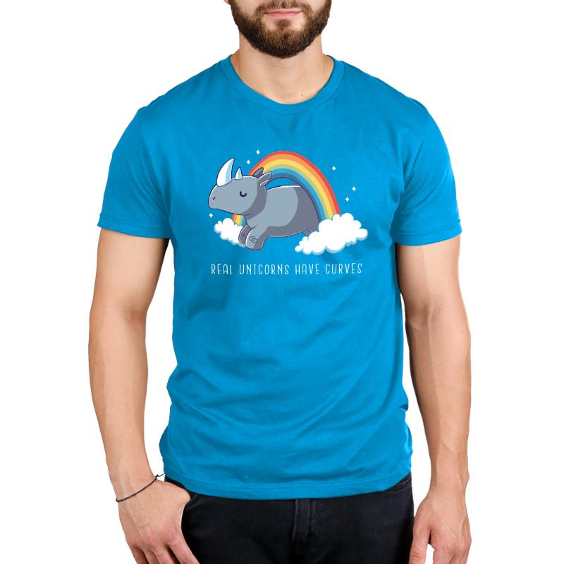 A man is wearing a cobalt blue Real Unicorns Have Curves by monsterdigital featuring an illustration of a rhinoceros on clouds with a rainbow and the text "Real Unicorns Have Curves." The shirt is made from super soft ringspun cotton.