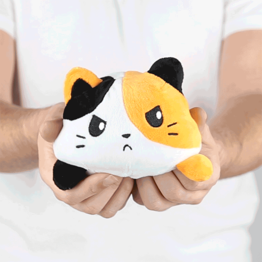 A person holding a TeeTurtle Reversible Cat Plushie (Calico) toy.