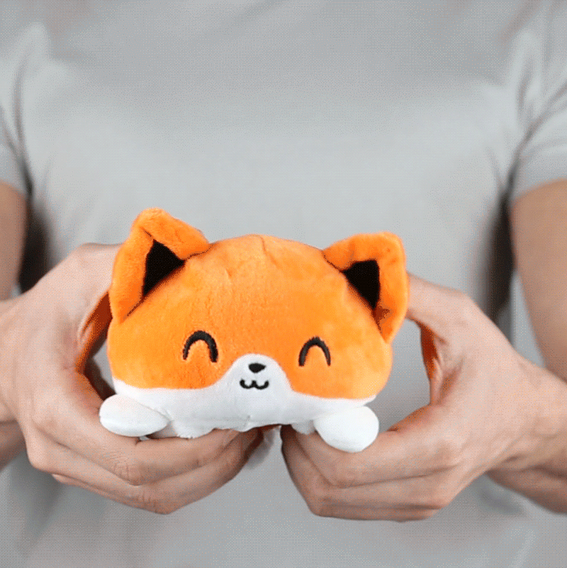 A person holding a TeeTurtle Reversible Fox Plushie (Orange) by TeeTurtle.