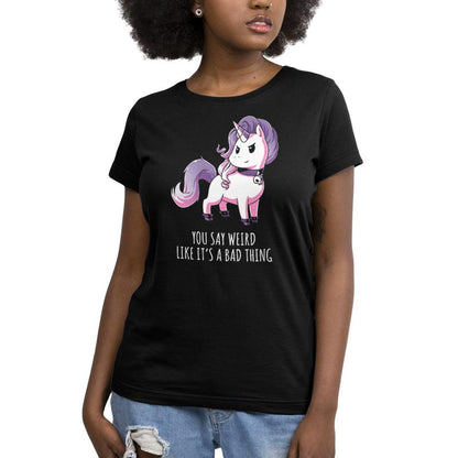 A person wearing a black monsterdigital T-shirt made of super soft ringspun cotton with a purple and white unicorn illustration and the text "Weird Is Good." They have curly hair and are also wearing ripped jeans.