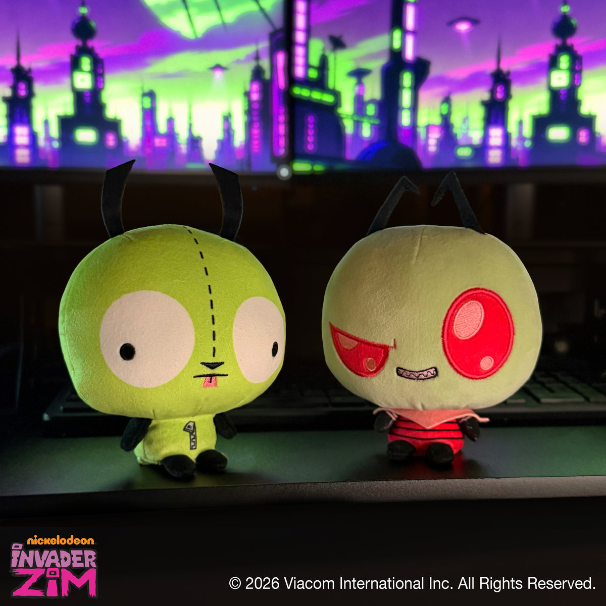 GIR and Zim Cloudheads plushies sitting together on a desk with a colorful green and purple cityscape in the background.